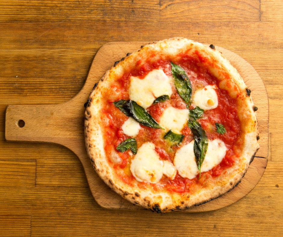 A birds eye shot of a margherita tomato pizza on a wooden serving board