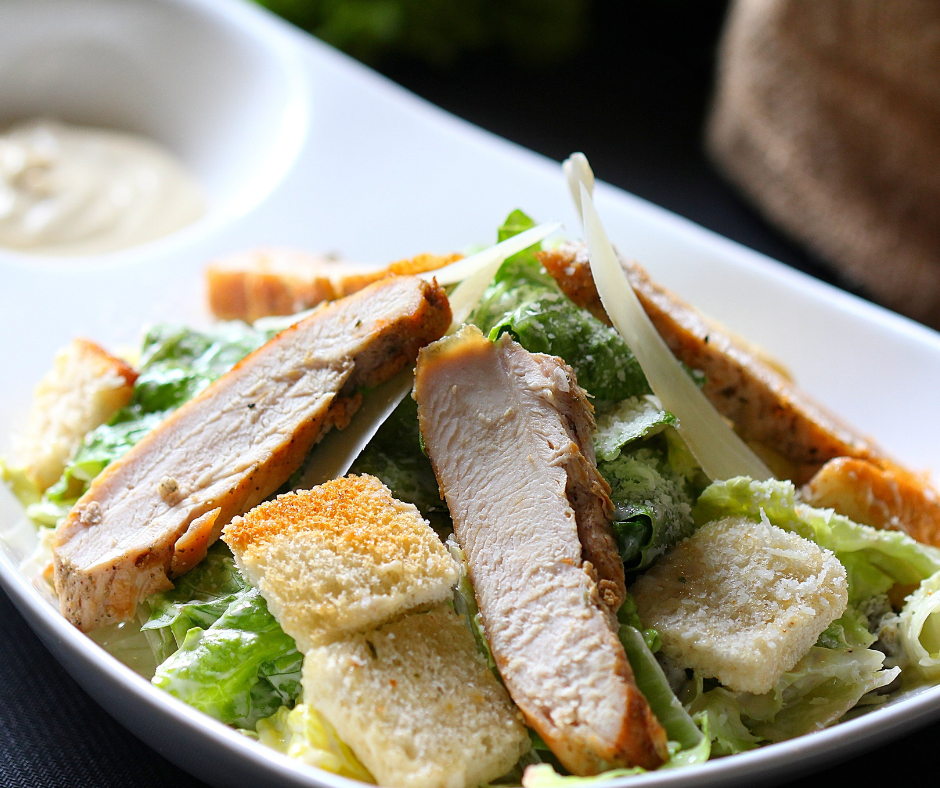 A close up of a chicken caesar salad in a bowl, with chicken, croutons, and romaine lettuce